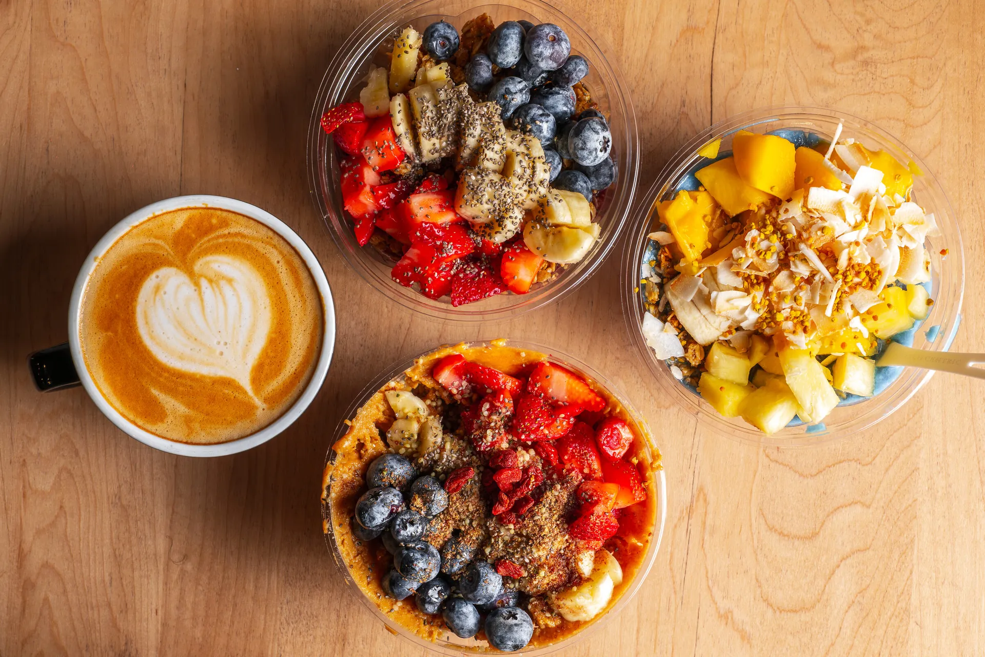 A latte and three açaí bowls on the wooden table at The Porch